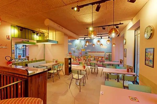 buffet, poubelles, tables roses , chaises vertes, spots, fresque murale colorée